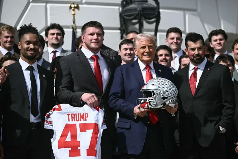US President Donald Trump, alongside defensive end Jack Sawyer (2nd L), wide receiever Emeka Egbuka (L), and head coach Ryan Day (R), holds an Ohio State Buckeyes football helmet as he hosts the 2025 College Football National Champions, Ohio State Buckeyes, celebrating the team's title-winning season with a ceremony on the South Lawn of the White House in Washington, DC, April 14, 2025. (Photo by Brendan SMIALOWSKI / AFP) (Photo by BRENDAN SMIALOWSKI/AFP via Getty Images)