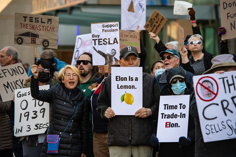 Protesters hold signs and sing chants during a protest against Elon Musk and his Tesla car company outside the Tesla dealership in Boston, Massachusetts on March 15, 2025. US President Donald Trump's senior advisor Elon Musk is leading the so-called Department of Government Efficiency (DOGE), which has cut thousands of government jobs and upended agencies, prompting numerous court challenges. (Photo by Joseph Prezioso / AFP) (Photo by JOSEPH PREZIOSO/AFP via Getty Images)
