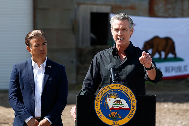 CERES, CALIFORNIA - APRIL 16: California Governor Gavin Newsom (R) speaks as California Attorney general Rob Bonta looks on during a news conference at Gemperle Orchard on April 16, 2025 in Ceres, California. Governor Gavin Newsom and California Attorney General Rob Bonta have filed a lawsuit in federal court challenging the Trump administration's use of emergency powers to enact sweeping tariffs that hurt states, consumers, and businesses. The tariffs have disrupted supply chains, increased costs for the state and Californians, and inflicted billions in damages on California’s economy, the fifth largest in the world. (Photo by Justin Sullivan/Getty Images)